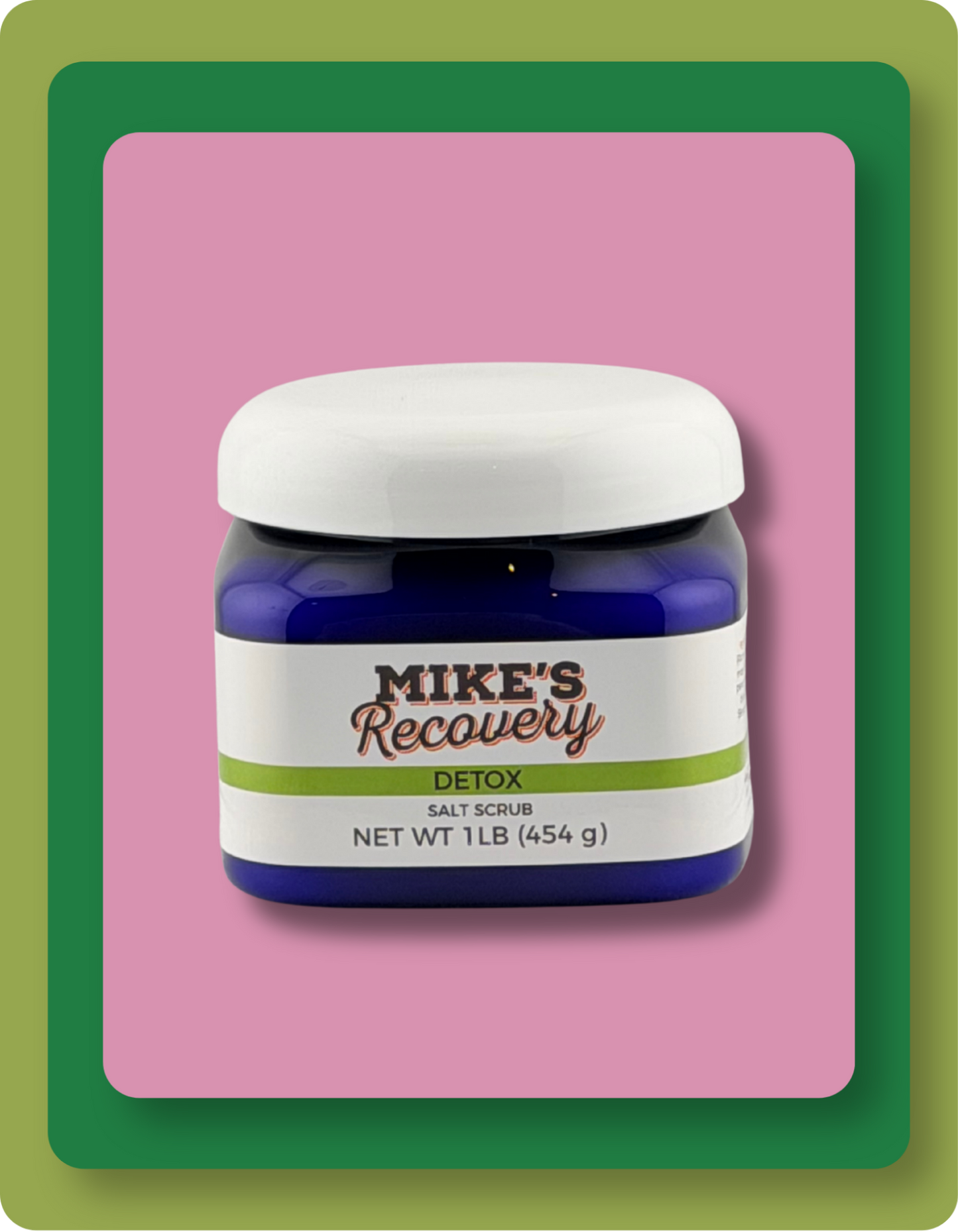 A jar of Mike's Recovery Detox Salt Scrub, featuring a dark blue container, a white lid, and a white label with green and grey  text, set against a pink background with green and orange borders.
