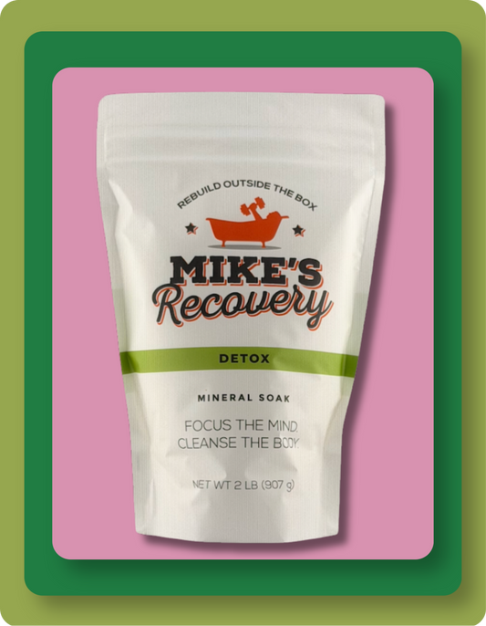 A stand-up pouch of Mike's Recovery Detox Mineral Soak, featuring a white bag with a green band and orange logo, set against a pink background with green and orange rounded borders.